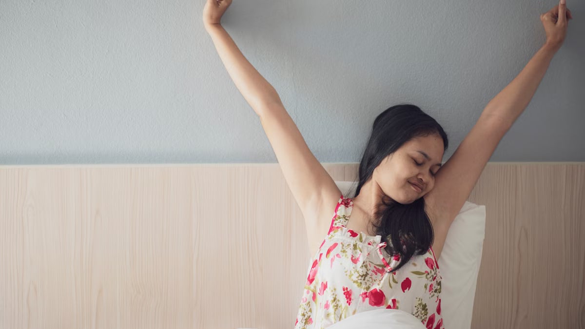 A woman joyfully stretching her arms while waking up in bed, feeling refreshed and energized.
