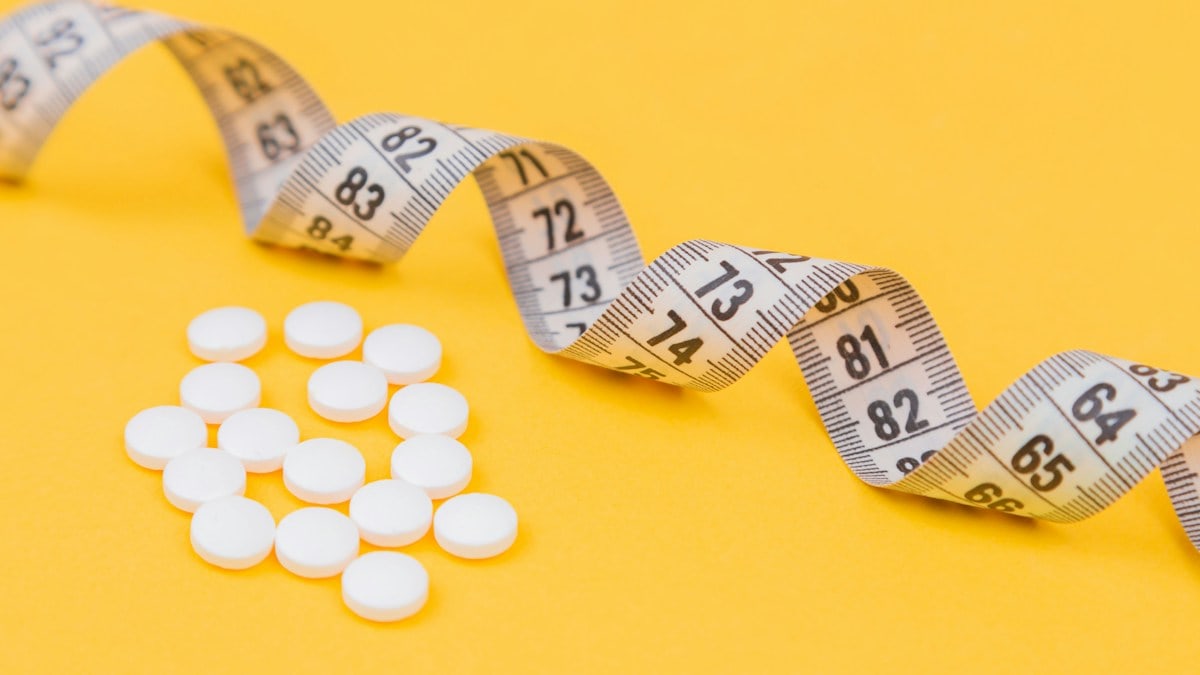 White measuring tape with a white pills, white vitamin on a yellow background. Diet. Slimming. Obesity. Place for an inscription. Weight loss marathon. Advertising. Top view. The close plan.